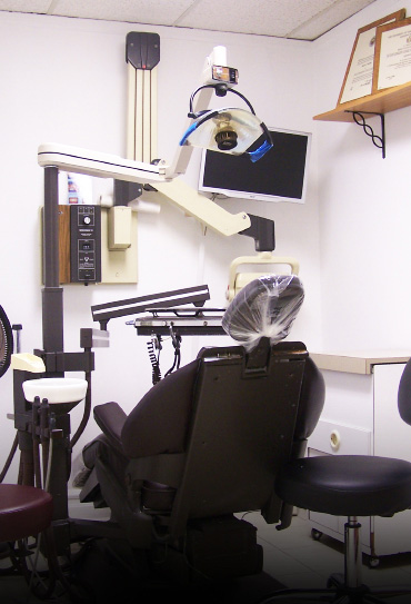 The image depicts a dental office setting with various pieces of equipment, including a dental chair, overhead lighting, and an examination table.