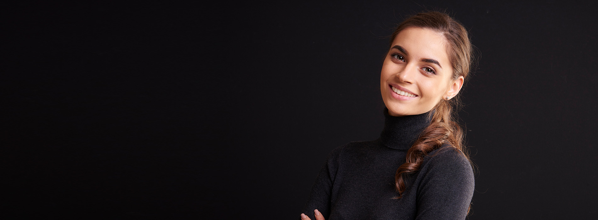 The image features a woman standing confidently with her arms crossed, smiling at the camera against a dark background.