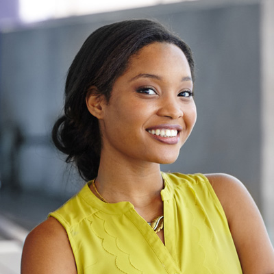 The image shows a woman with a radiant smile, posing confidently against a blurred background.