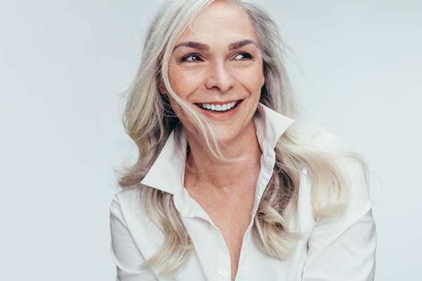 A woman with short blonde hair, wearing a white top and a necklace, smiling at the camera.