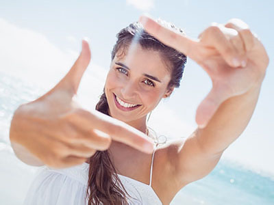 A woman with long hair holding up two fingers against a bright background.