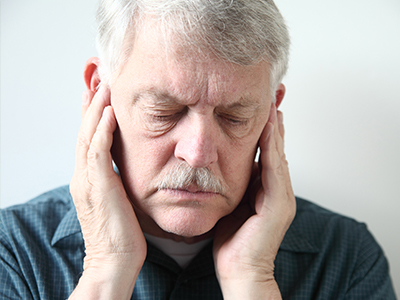 This is a photograph of an elderly man with closed eyes, his hand placed on the side of his face, possibly indicating pain or discomfort.