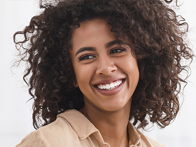 The image depicts a smiling person with curly hair, wearing a light-colored top, against a plain background.